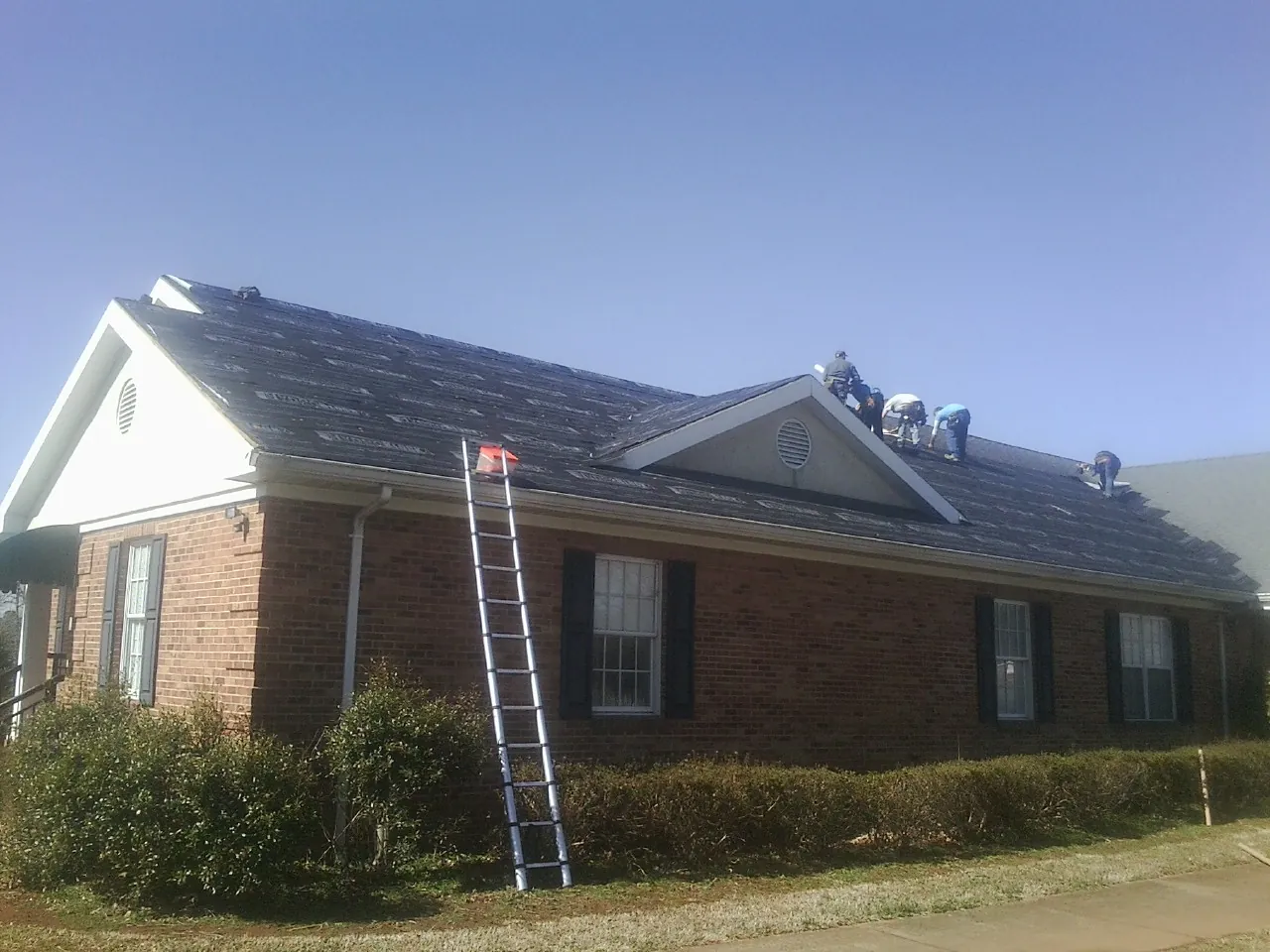 Crew tearing shingles off a brick ranch roof with a ladder set — Emergency Roof Repair work by our crew in New Meadows
