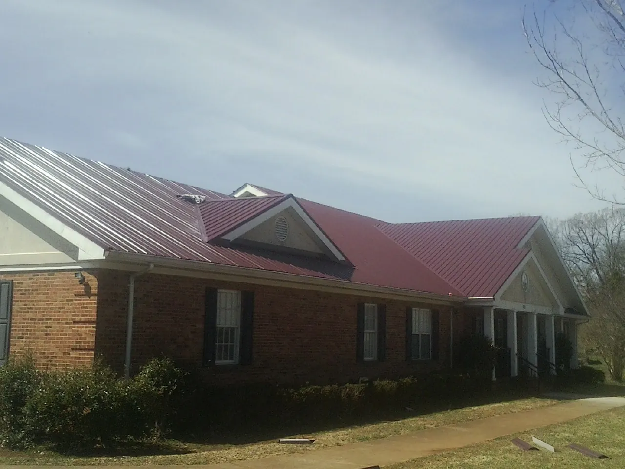 Red metal roof with gabled entries on a long brick building, from a Hail Damage Roof Repair job in New Meadows