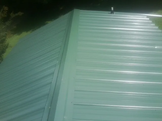 New green metal panels meeting at the ridge of a roof — Flat Roof Repair work by our crew in New Meadows