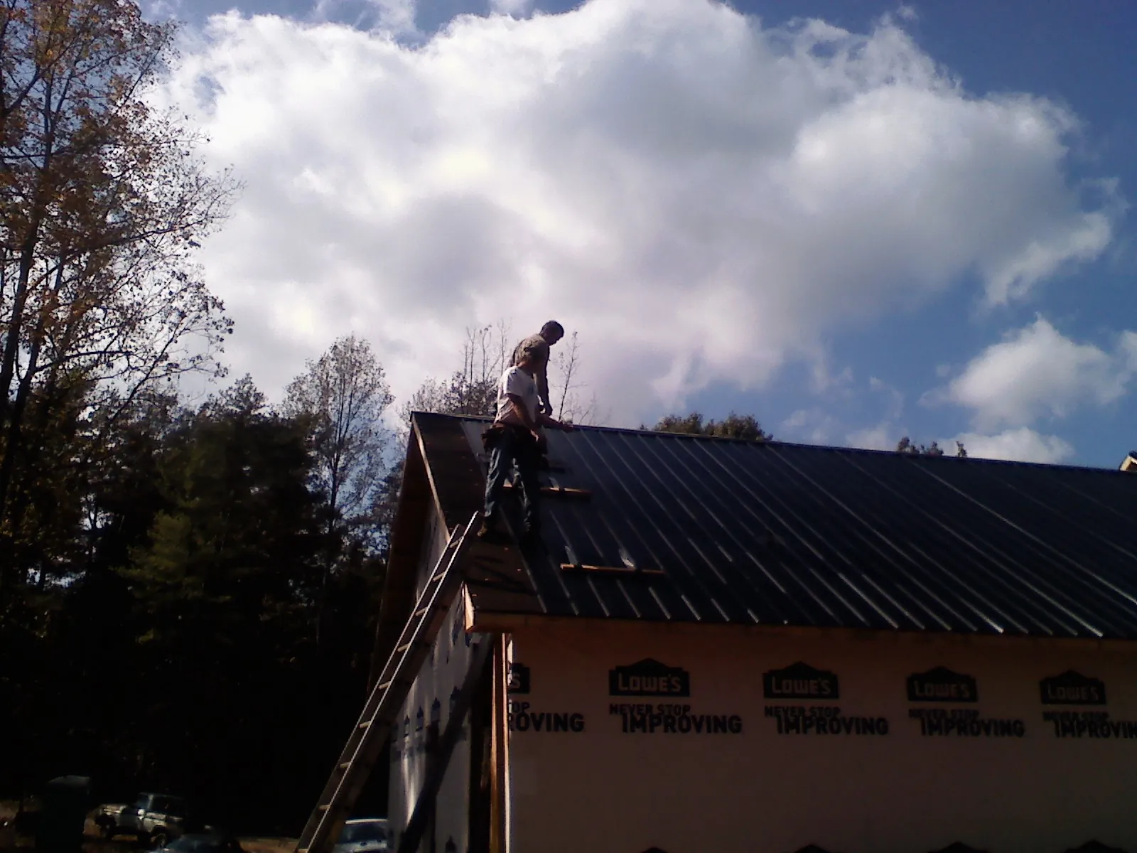 Roofer fastening dark metal panels high against a cloudy sky, from a Roof Inspection job in New Meadows