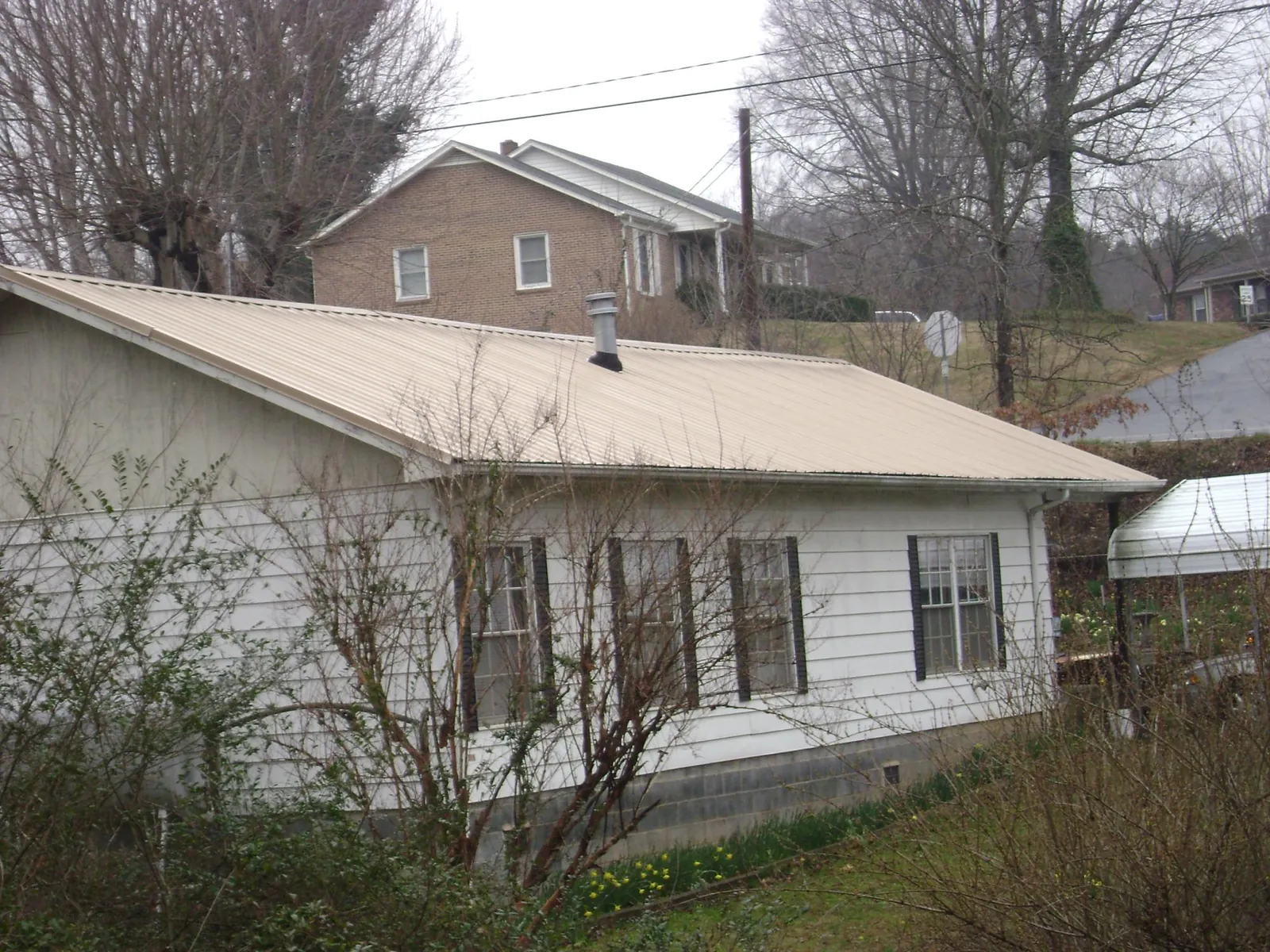 Tan metal roof on a white sided house set into a hillside — Commercial Roofing by Roofing Brothers in New Meadows